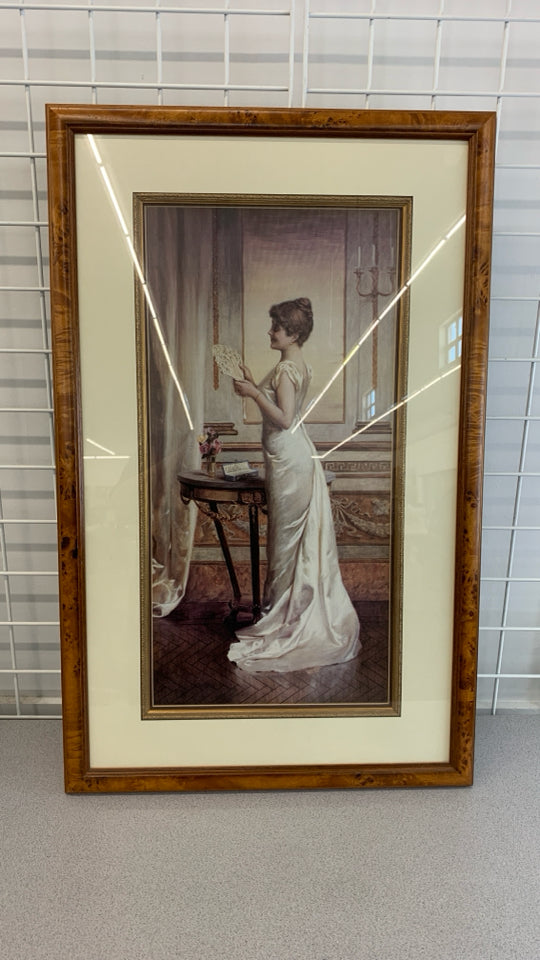 WOMAN HOLDING FAN IN BROWN WOOD FRAME.
