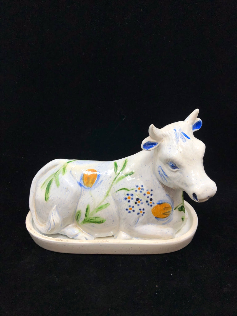 CERAMIC COW COVERED BUTTER DISH W/BLUE & YELLOW FLORAL MOTIFS.