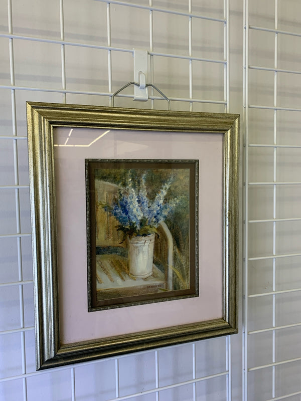 BLUE FLOWERS IN WHITE PLANTER W/ SILVER FRAME WALL HANGING.