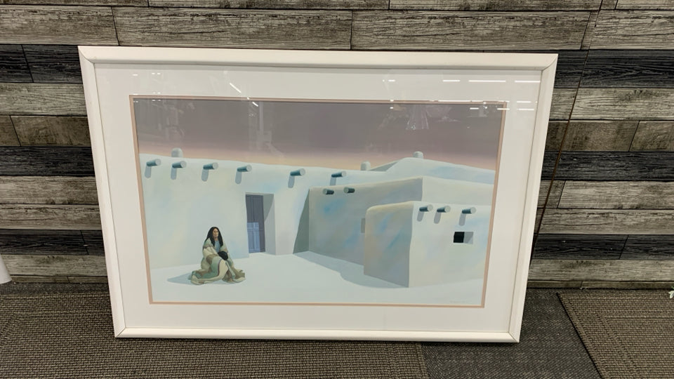 WOMAN SITTING W/WHITE SOUTHWESTERN HOME PAINTING IN WHITE FRAME.