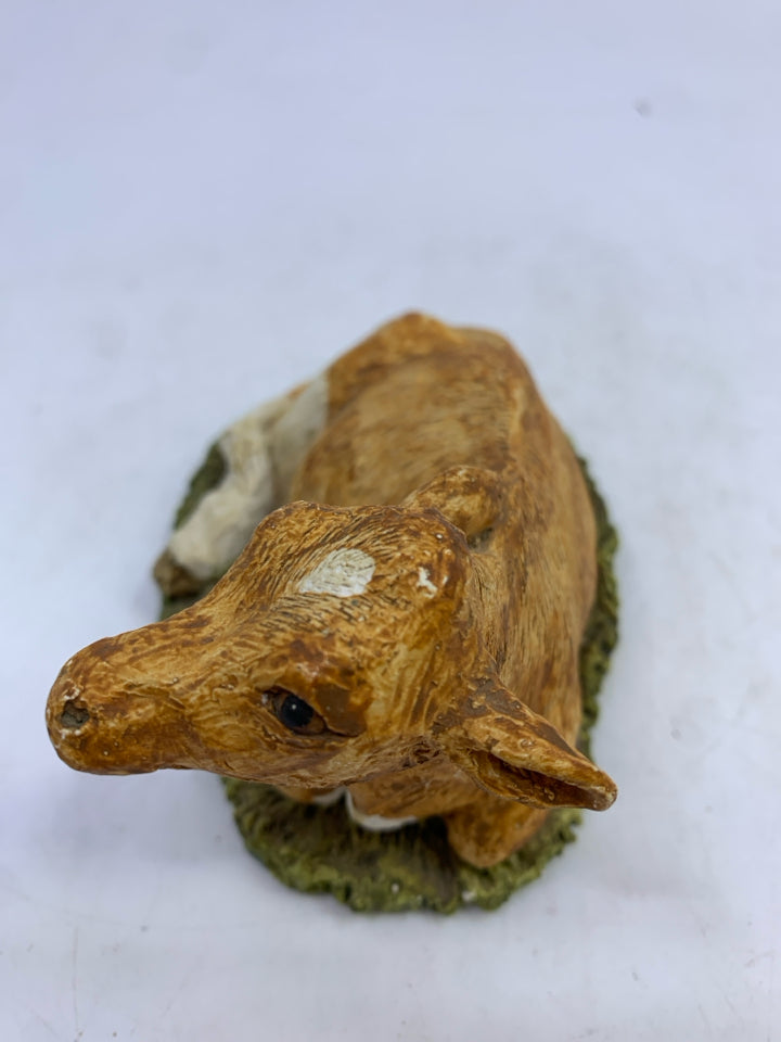 CERAMIC SITTING LIGHT BROWN/WHITE COW ON GRASS.