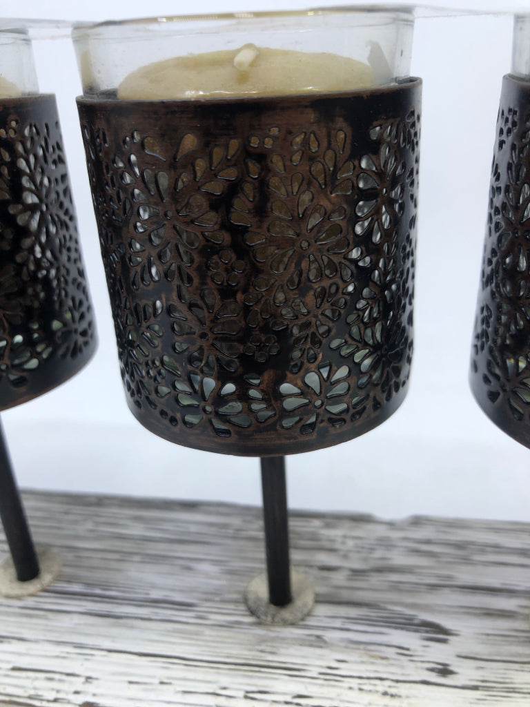 5 METAL CANDLE HOLDERS ON DISTRESSED WOOD BLOCK.