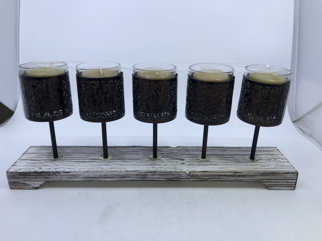 5 METAL CANDLE HOLDERS ON DISTRESSED WOOD BLOCK.
