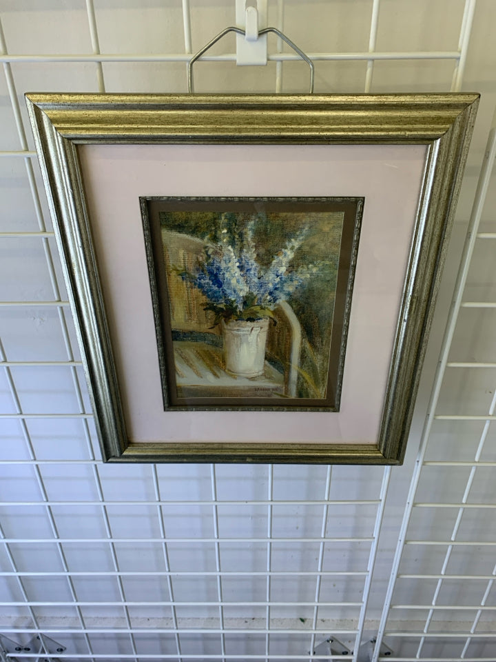 BLUE FLOWERS IN WHITE PLANTER W/ SILVER FRAME WALL HANGING.