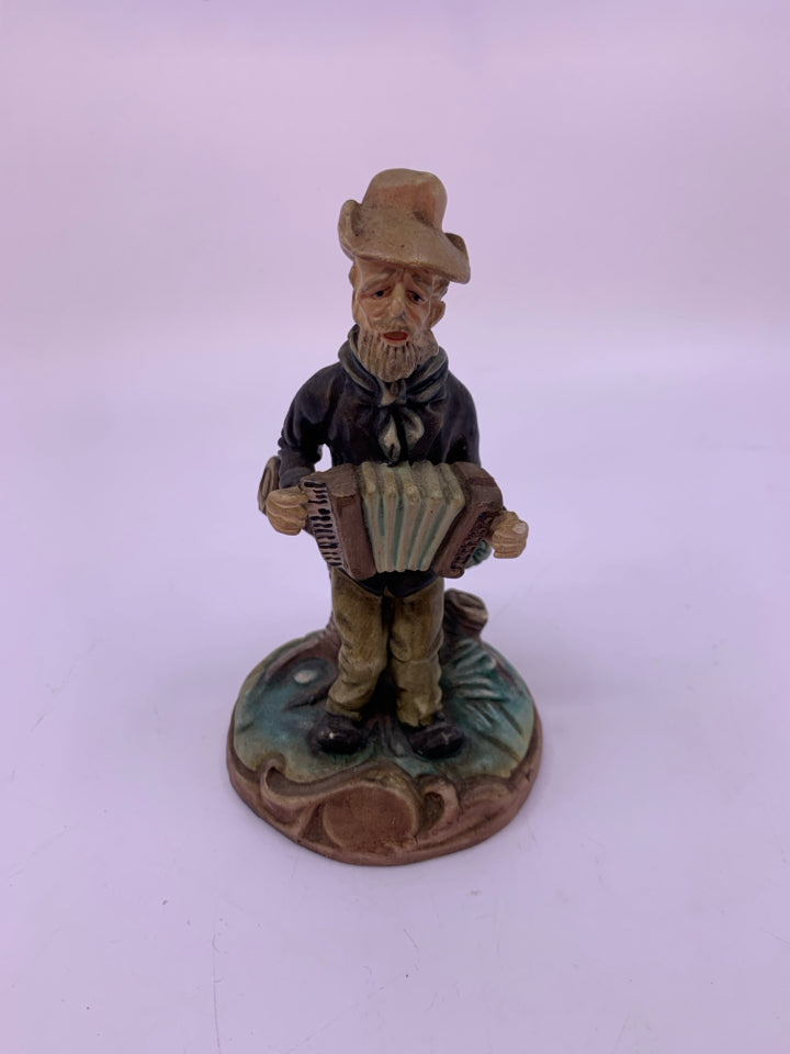 MAN PLAYING ACCORDION LEANING ON TREE.