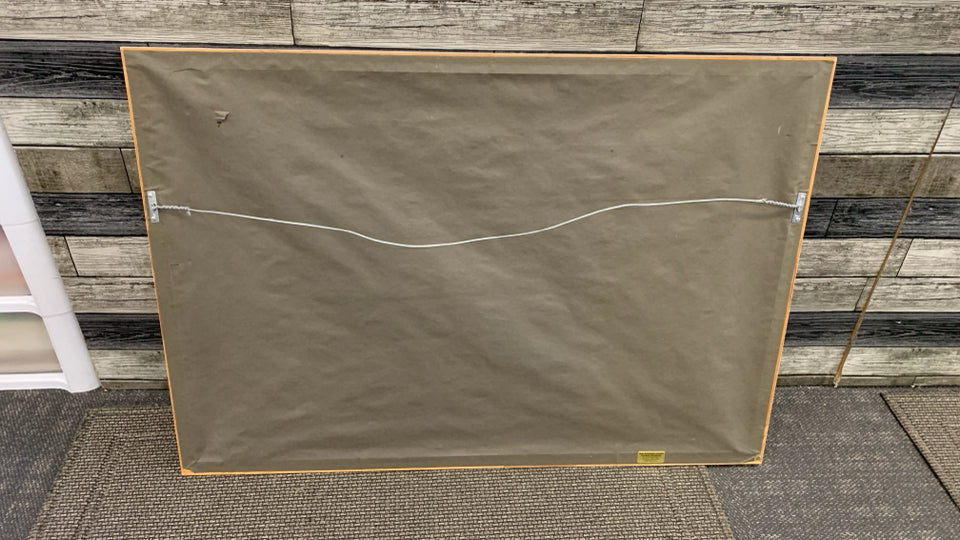 WOMAN SITTING W/WHITE SOUTHWESTERN HOME PAINTING IN WHITE FRAME.