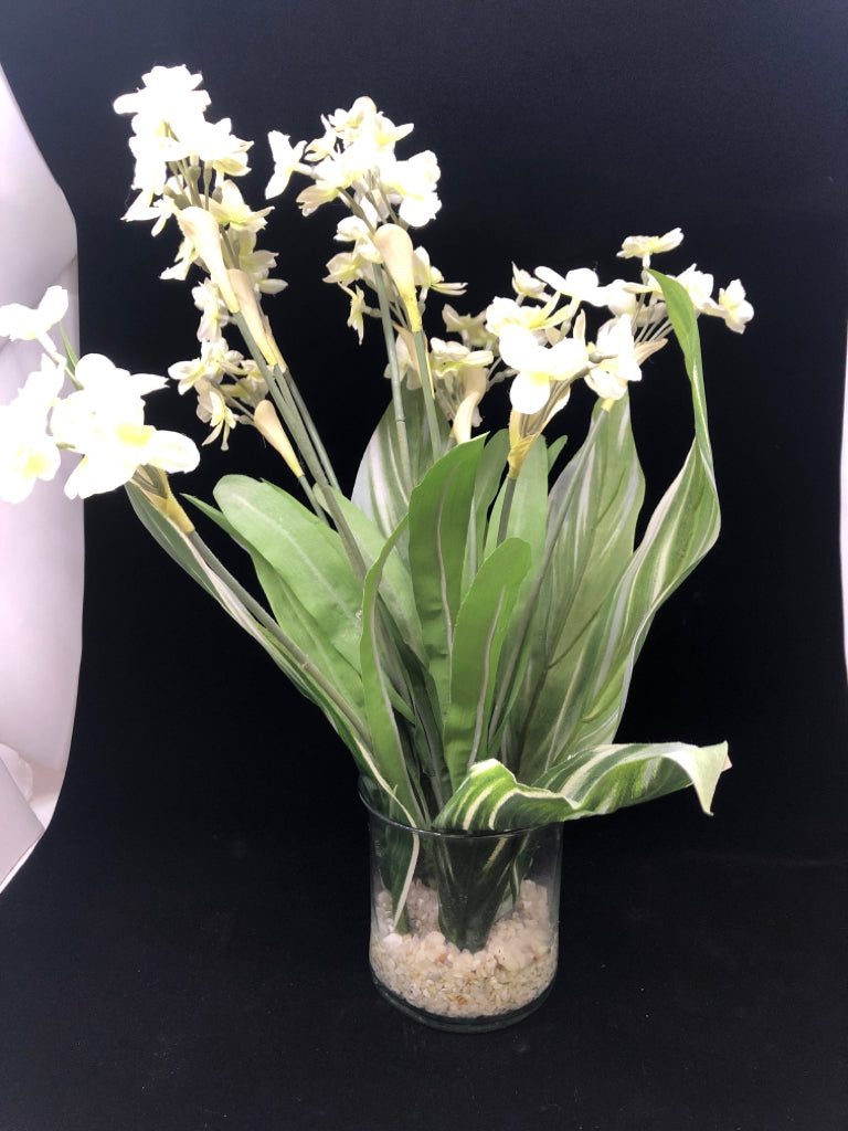 FAUX LEAVES W/ WHITE FLOWERS IN CLEAR VASE W/ WHITE ROCKS.