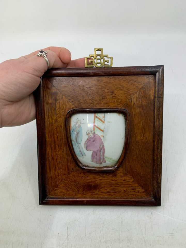 WOOD WALL HANGING W/ 2 MEN LOOKING AT EACHOTHER POTTERY PIECE.