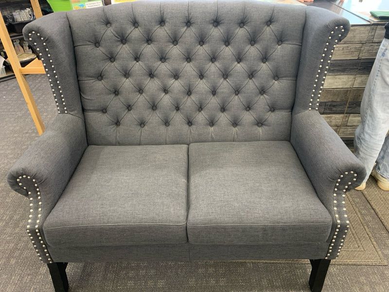 DARK GRAY WING BACK TUFTED LOVE SEAT WITH NAIL HEAD DETAILS.