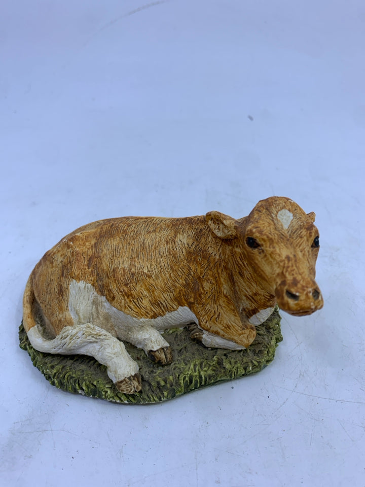 CERAMIC SITTING LIGHT BROWN/WHITE COW ON GRASS.