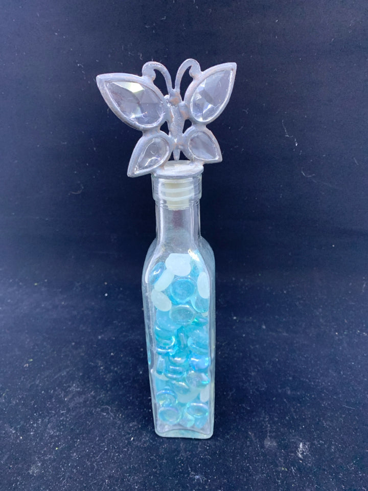 GLASS BOTTLE WITH BLUE AND WHITE STONES AND BUTTERFLY STOPPER.