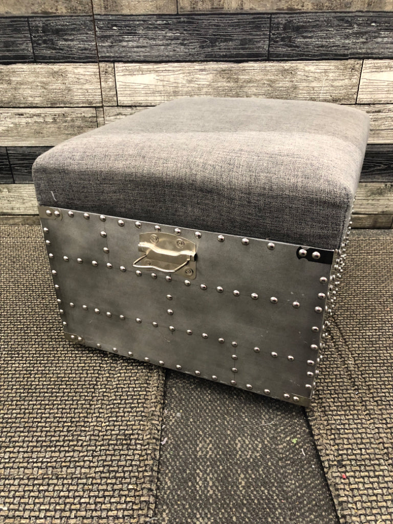SMALL GREY STUDDED OTTOMAN W METAL HANDLES AND STORAGE.
