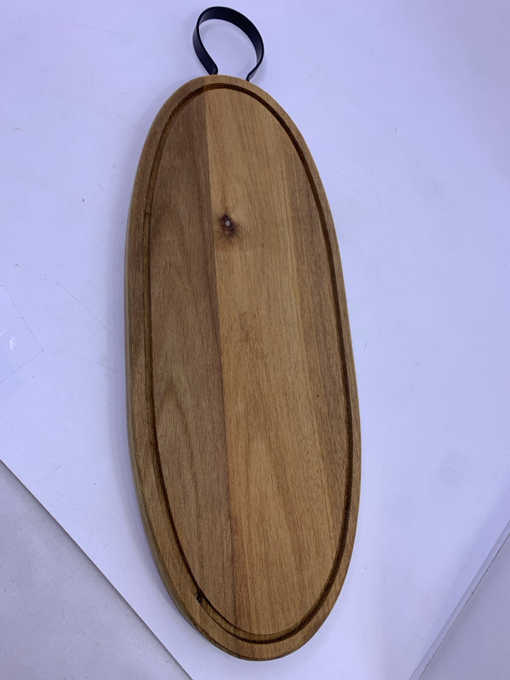 OVAL WOOD CUTTING BOARD WITH BLACK METAL HANDLE.