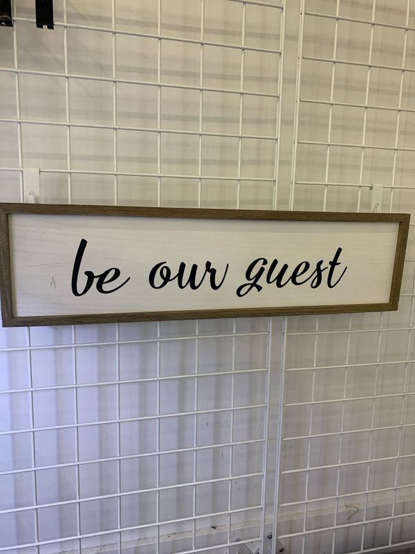"BE OUR GUEST" BLACK LETTERS ON WHITE SIGN.