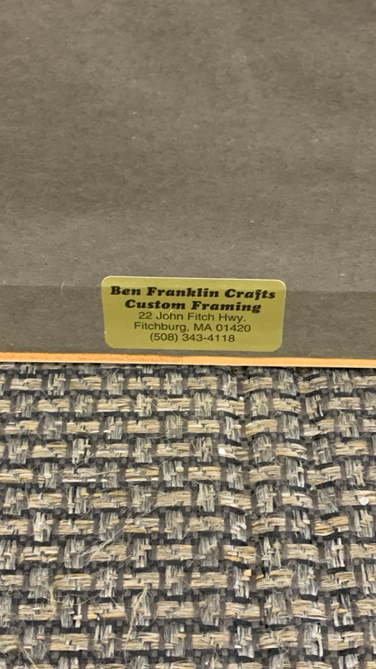 WOMAN SITTING W/WHITE SOUTHWESTERN HOME PAINTING IN WHITE FRAME.