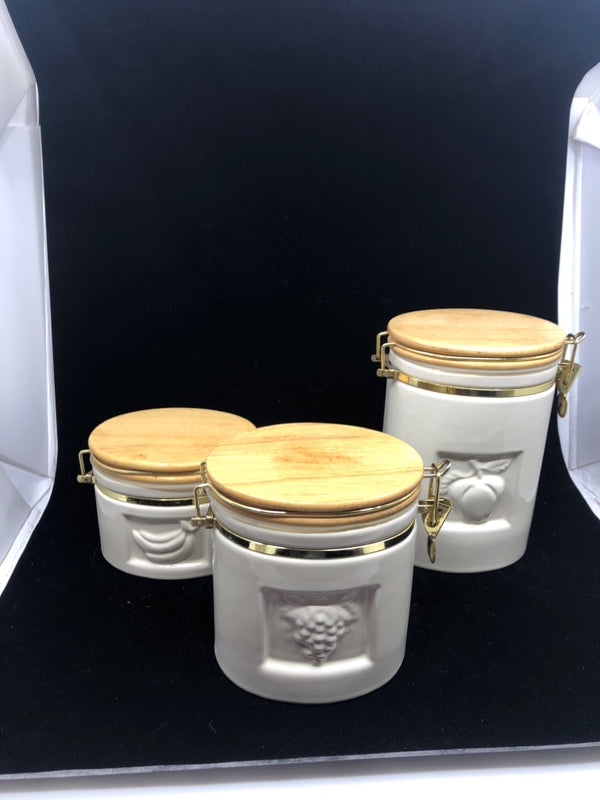 3 OVAL CREAM CERAMIC CANISTERS W/ WOOD TOPS EMBOSSED FRUITS.