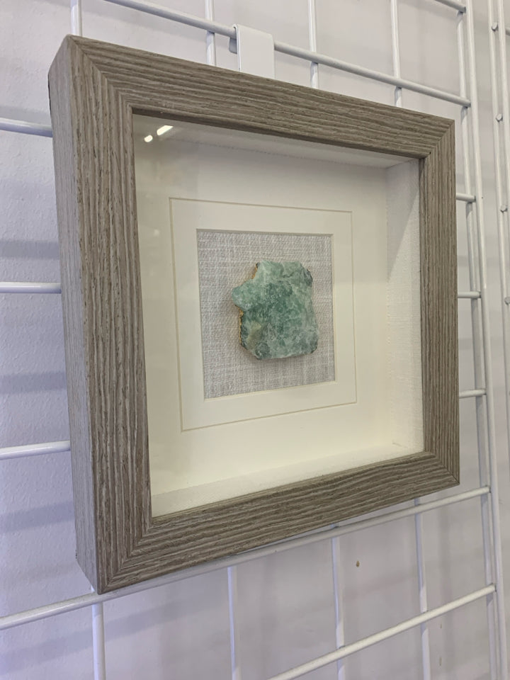 GREEN CRYSTAL IN SHADOW BOX WITH GRAY FRAME.