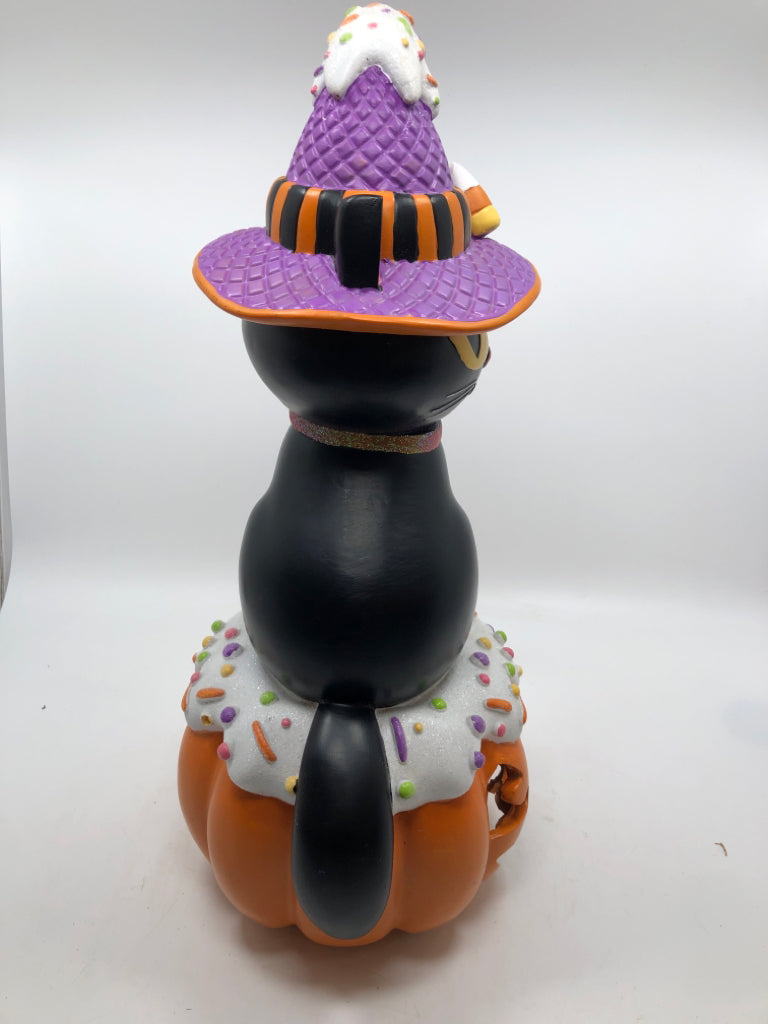 BLACK CAT W/ CANDY HAT SITTING ON LIGHT UP JACKO LANTERN.