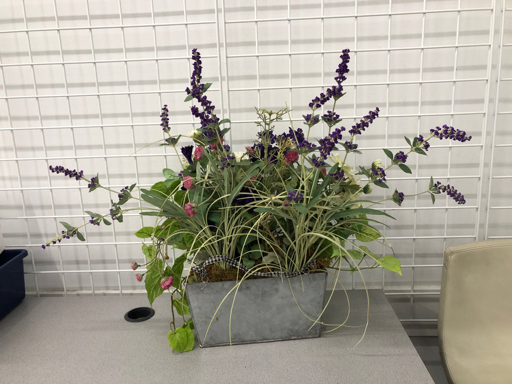 FAUX PURPLE FLOWERS IN GALVANIZED TIN WALL POCKET.