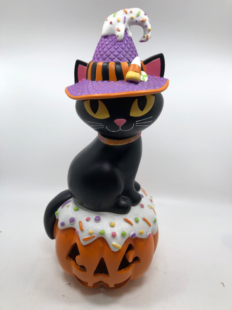 BLACK CAT W/ CANDY HAT SITTING ON LIGHT UP JACKO LANTERN.