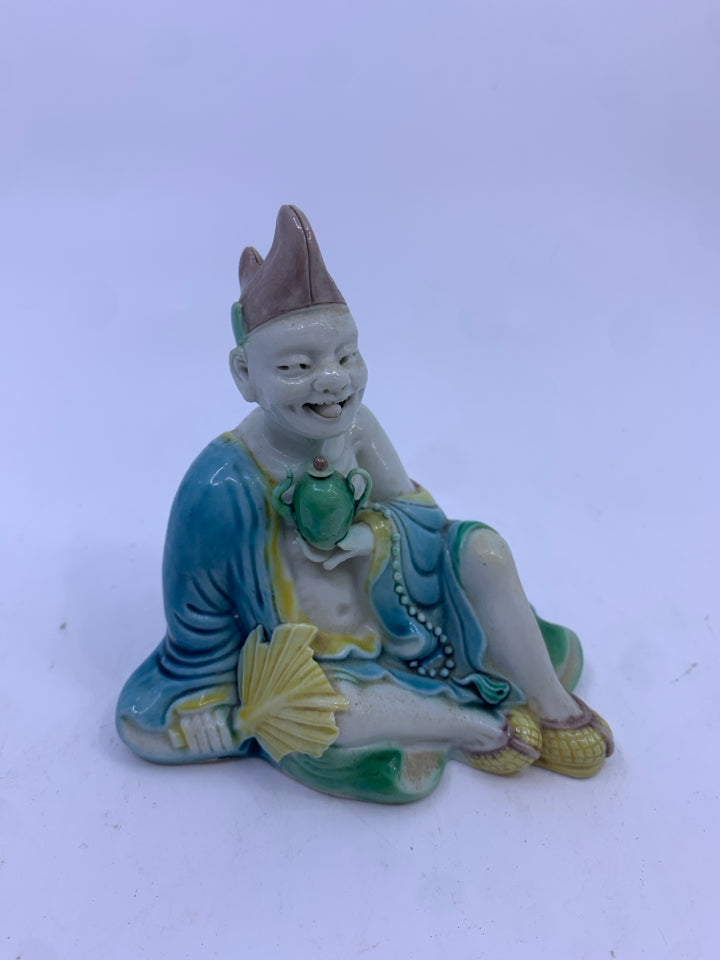 ASIAN MAN IN BLUE HOLDING TEAPOT SITTING.