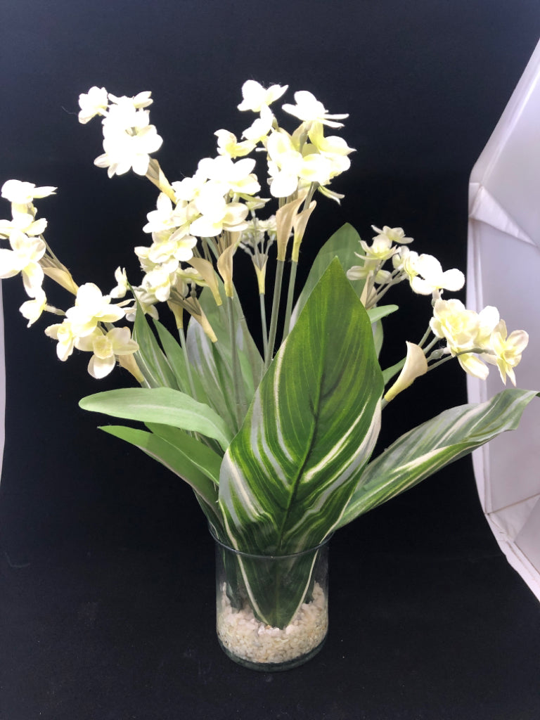 FAUX LEAVES W/ WHITE FLOWERS IN CLEAR VASE W/ WHITE ROCKS.