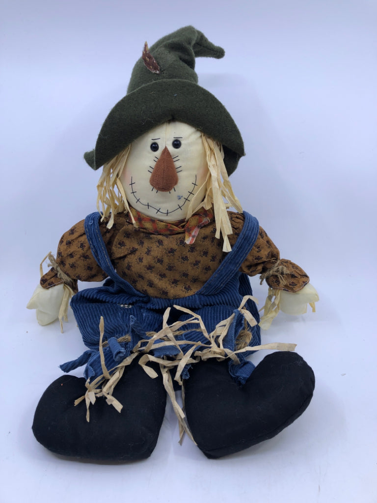 SHELF SITTING SCARECROW IN OVERALLS.