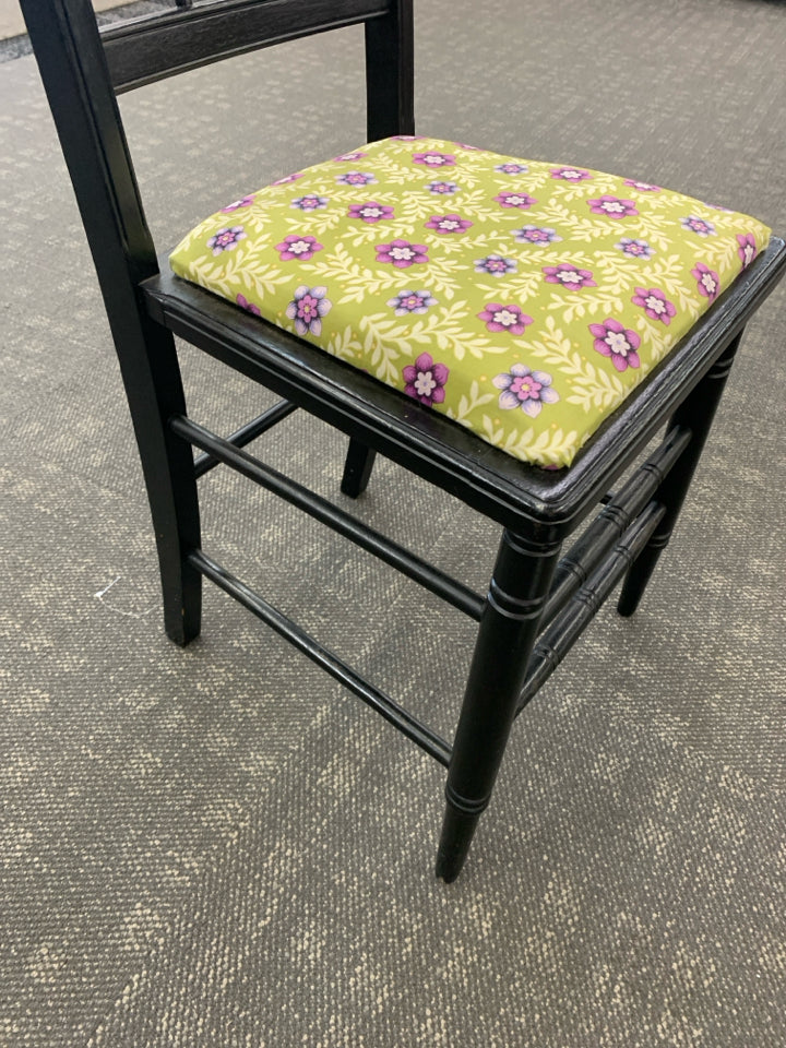 SMALL BLACK DESK WITH DRAWER AND BLACK CHAIR W/ GREEN AND PURPLE FLORAL CUSHION.