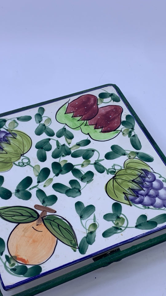 FRUIT PAINTED CERAMIC TRIVET ON GREEN METAL STAND.