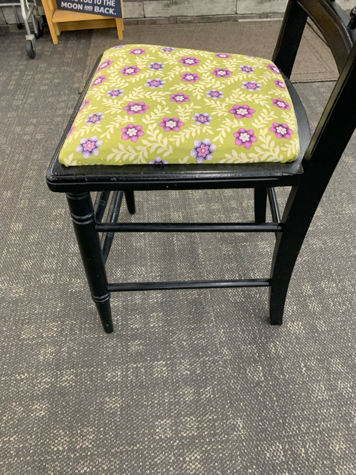 SMALL BLACK DESK WITH DRAWER AND BLACK CHAIR W/ GREEN AND PURPLE FLORAL CUSHION.