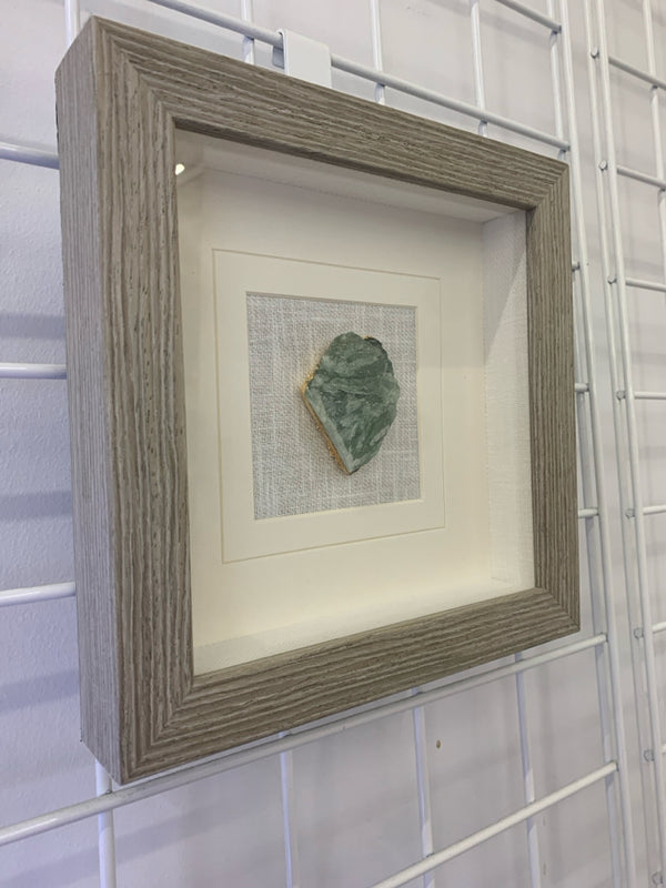 GREEN SQUARE CRYSTAL IN SHADOW BOX WITH GRAY FRAME.