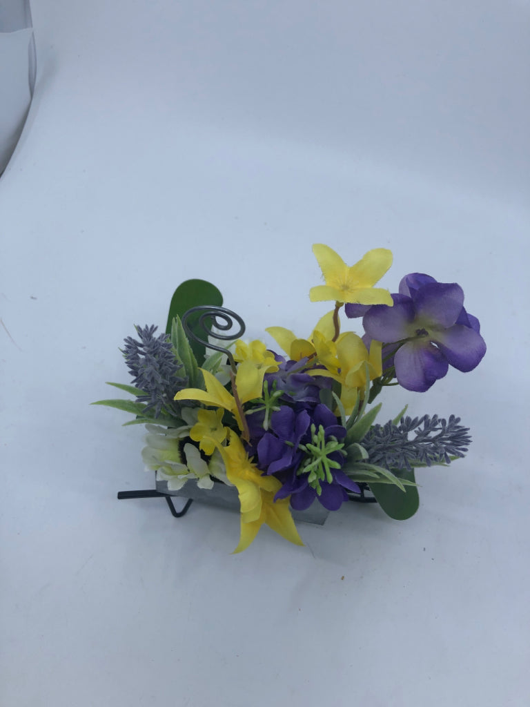 FAUX YELLOW AND PURPLE FLOWERS IN METAL WHEEL BARROW.