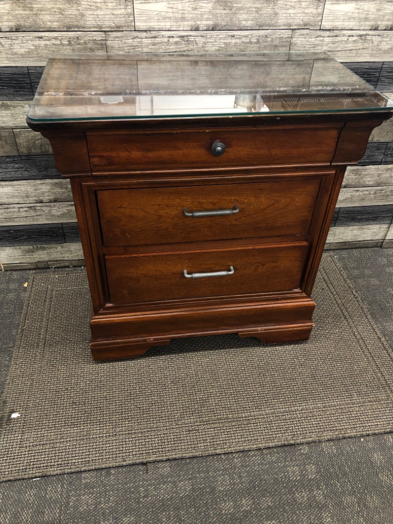 DARK CHERRY SIDE TABLE W/VTG METAL HANDLES & GLASS COVER ON WHEELS.