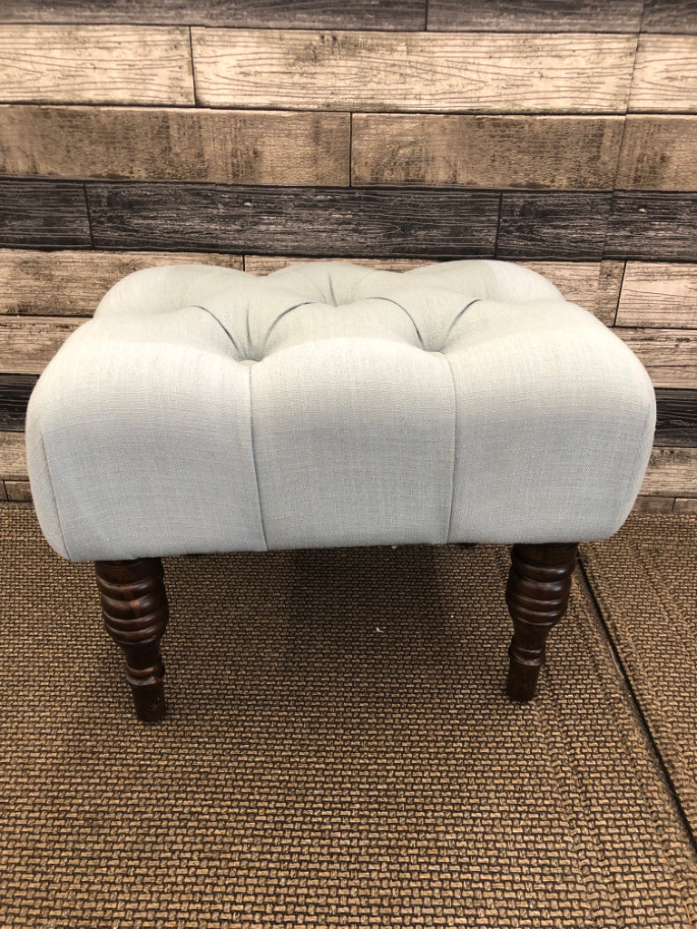 LIGHT BLUE BUTTON DETAIL OTTOMAN W/ BLACK LEGS.