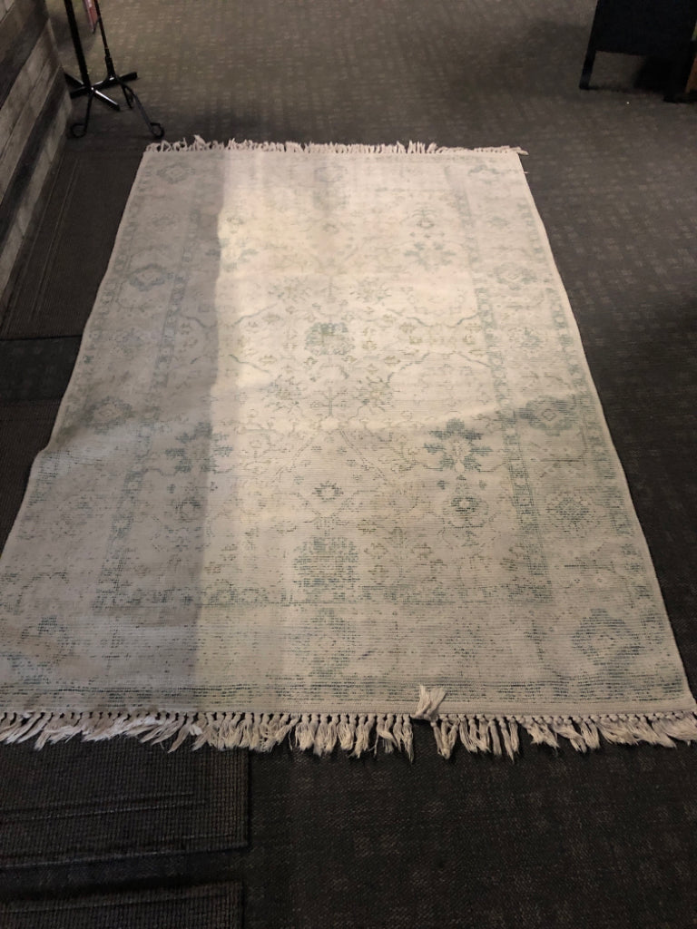 CREAM RUG W/ FADED LOOK GREEN PATTERN W/ TASSELS.