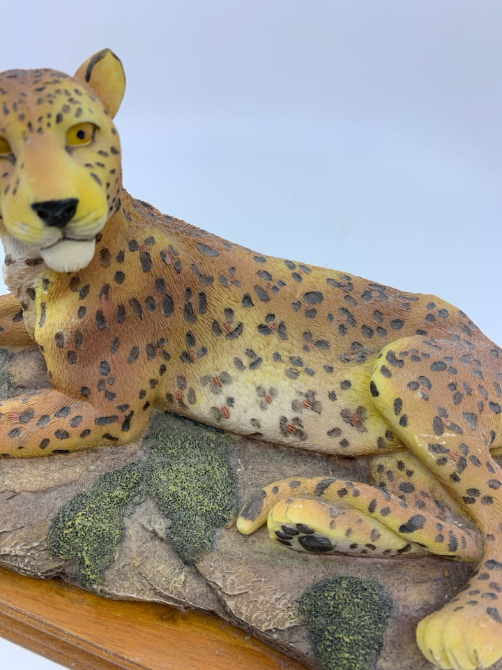 LEOPARD LAYING DOWN ON WOOD BASE.