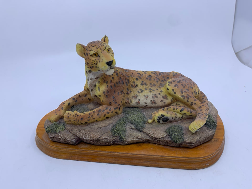 LEOPARD LAYING DOWN ON WOOD BASE.