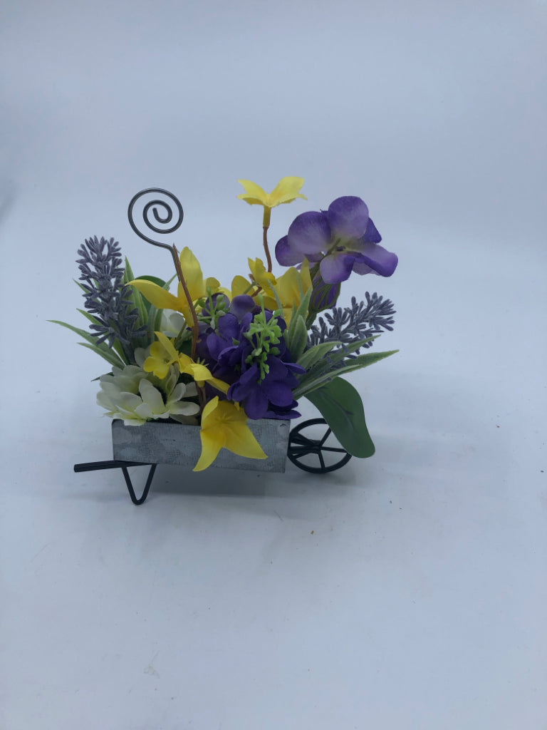 FAUX YELLOW AND PURPLE FLOWERS IN METAL WHEEL BARROW.