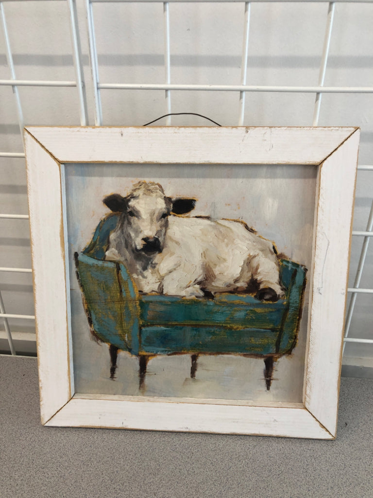 COW ON COUCH PAINTED WOOD IN WHITE WOOD FRAME.