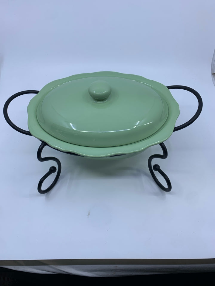 GREEN CASSEROLE DISH W LID AND BLACK METAL STAND.