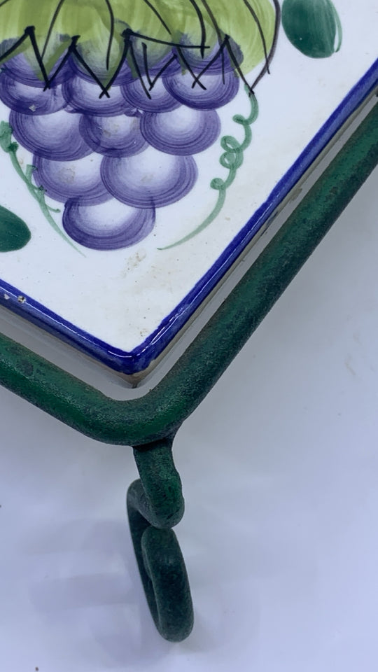 FRUIT PAINTED CERAMIC TRIVET ON GREEN METAL STAND.