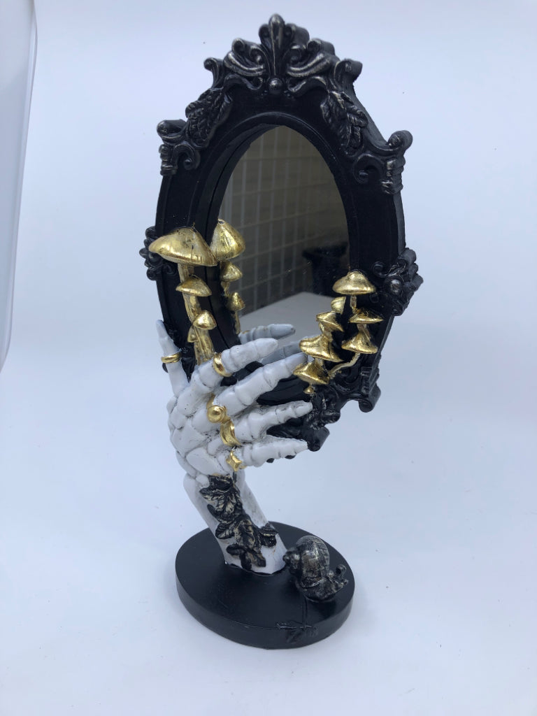 RESIN SKELTON HAND HOLDING BLACK MIRROR W/ GOLD MUSHROOMS.