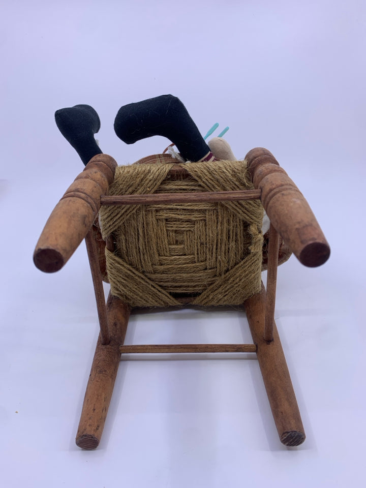 PRIMITIVE GIRL W/BASKET OF YARN SITTING IN A CHAIR.