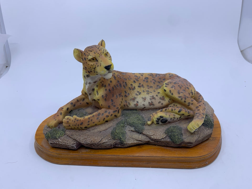 LEOPARD LAYING DOWN ON WOOD BASE.