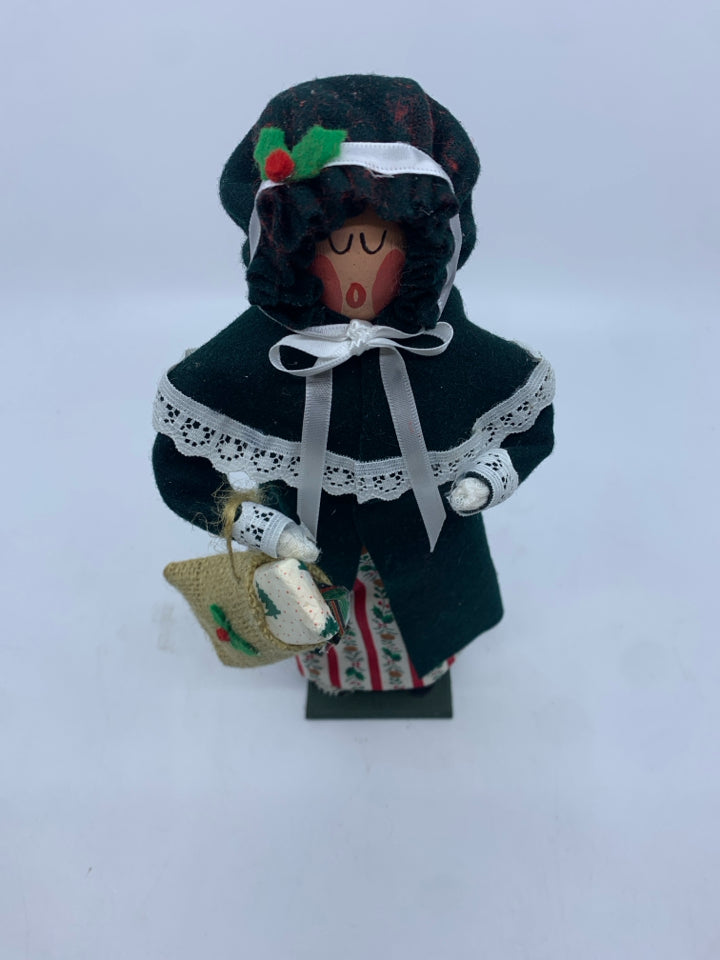 COUNTRY CAROLERS WOMAN IN GREEN COAT HOLDING SACK OF GIFTS.