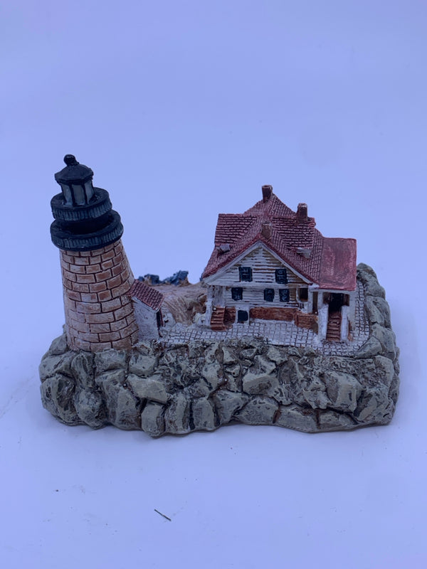 BRICK LIGHT HOUSE WITH WHITE HOUSE AND ROCKS.